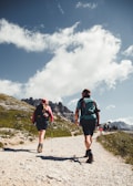 man in green shirt and black shorts with hiking backpack walking on gray sand during daytime