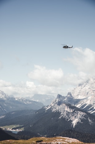 A sleek helicopter flying over a mountainous landscape under clear skies.