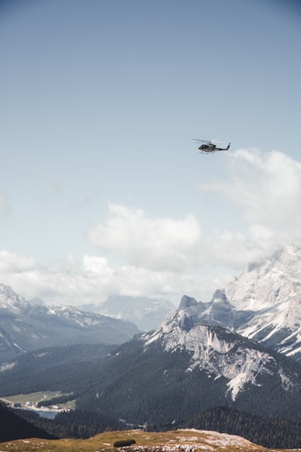 A sleek helicopter flying over a mountainous landscape under clear skies.