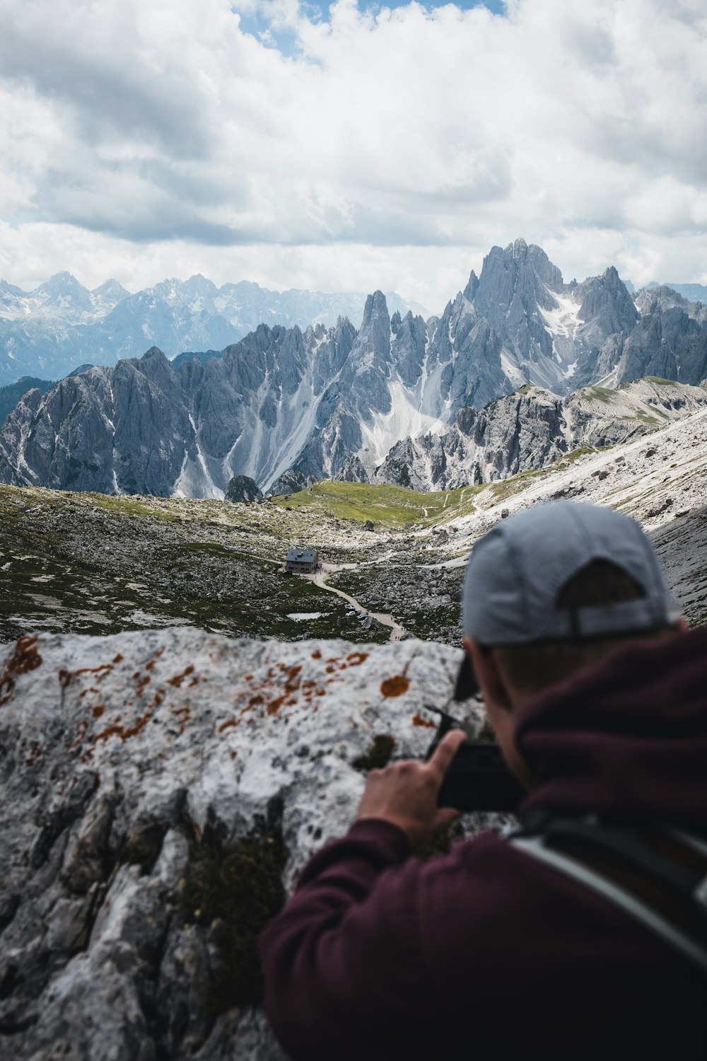 person in gray jacket and black cap sitting on rock mountain during daytime