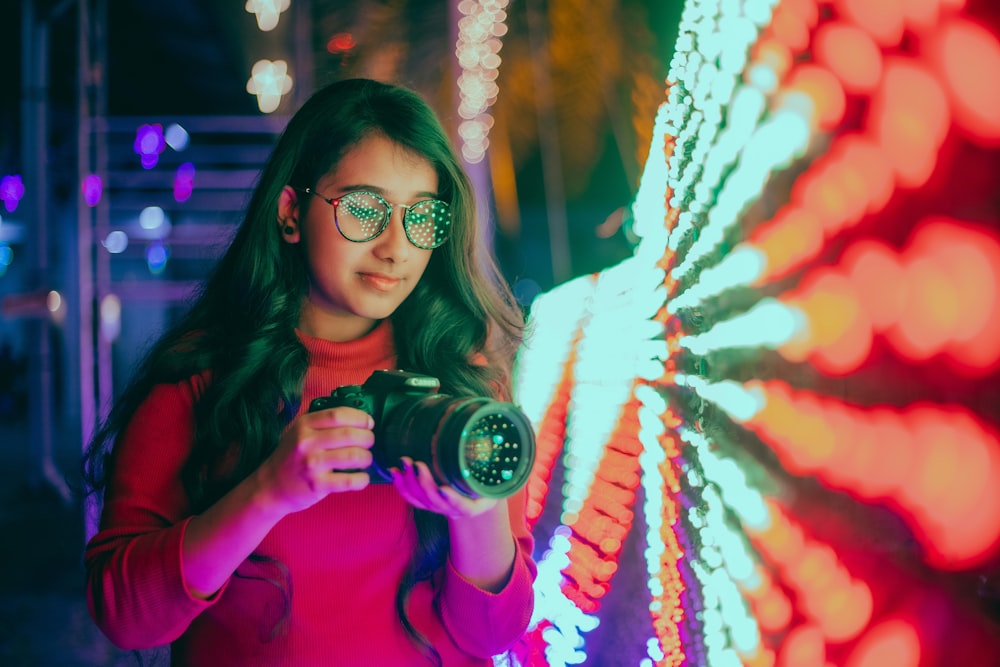 woman in pink long sleeve shirt holding black dslr camera