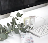 A clean, editorial-style desk featuring a warm gray keyboard, a cream mouse pad, and a delicate candle.