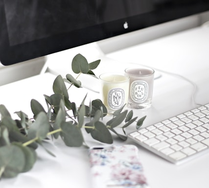 A serene workspace with a minimalist desk, a sleek laptop, and a delicate fragrance bottle beside a soft candle.