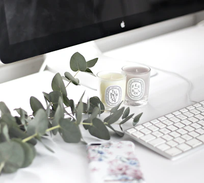 A clean, editorial-style desk featuring a warm gray keyboard, a cream mouse pad, and a delicate candle.