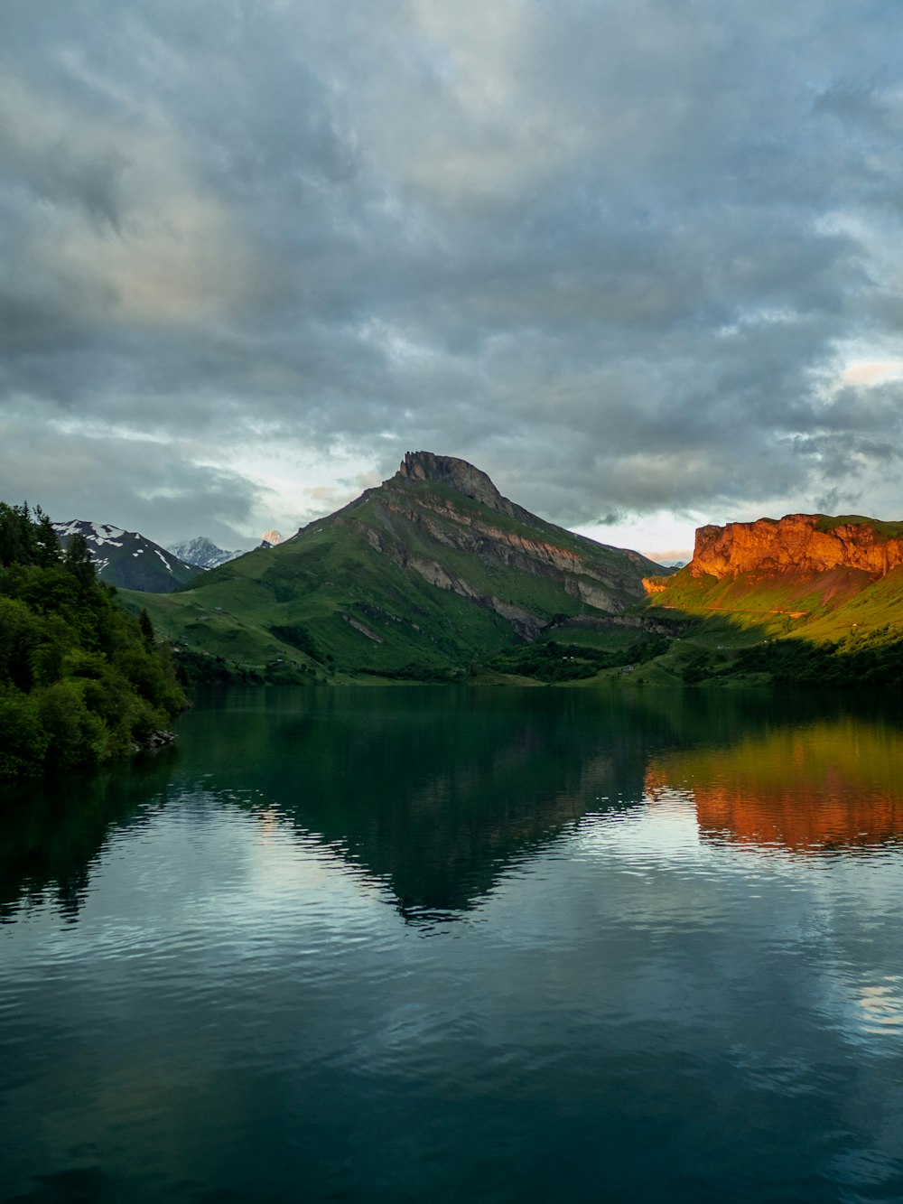 green and brown mountain beside lake under cloudy sky during daytime