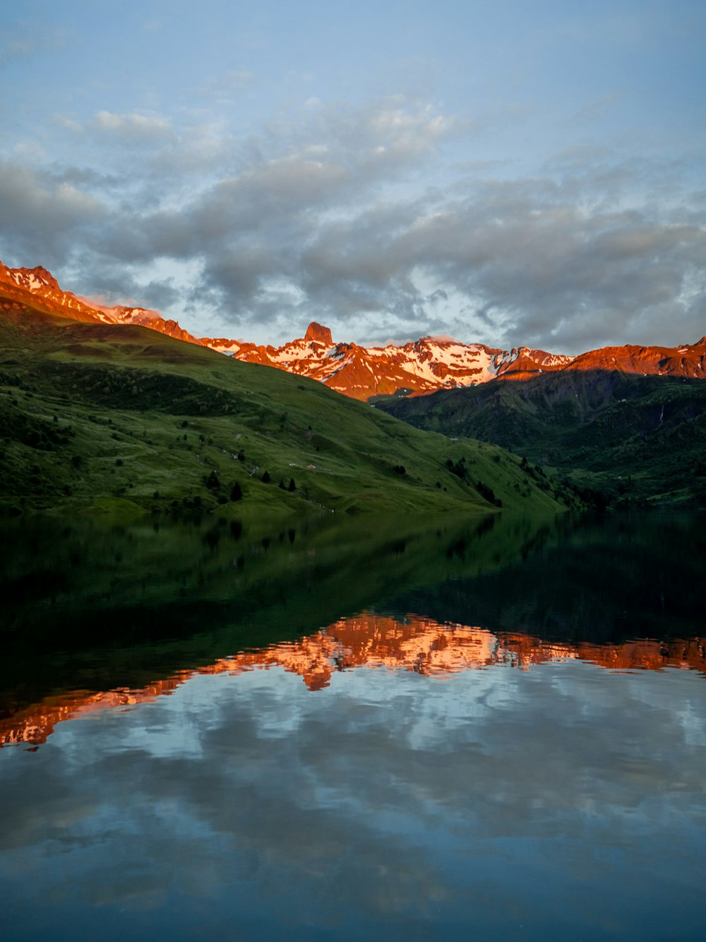 montanhas verdes ao lado do lago sob o céu nublado durante o dia