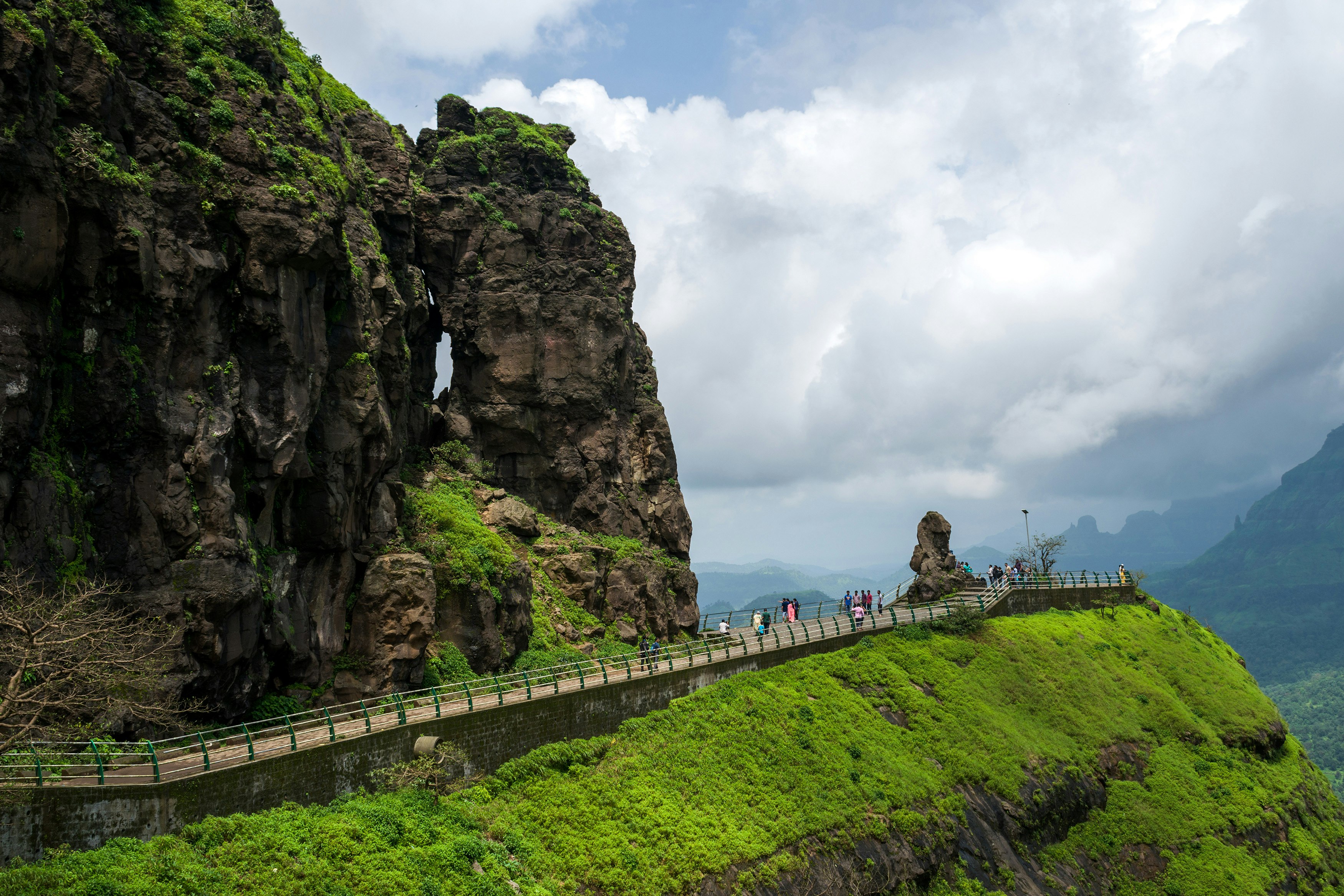 people walking on gray concrete bridge near brown rock formation during daytime