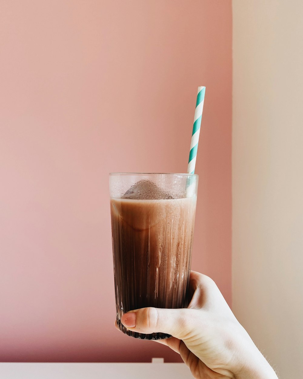 person holding clear drinking glass with brown liquid