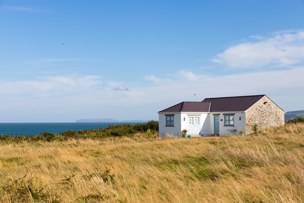 maison blanche et grise sur le champ d’herbe verte sous le ciel bleu pendant la journée