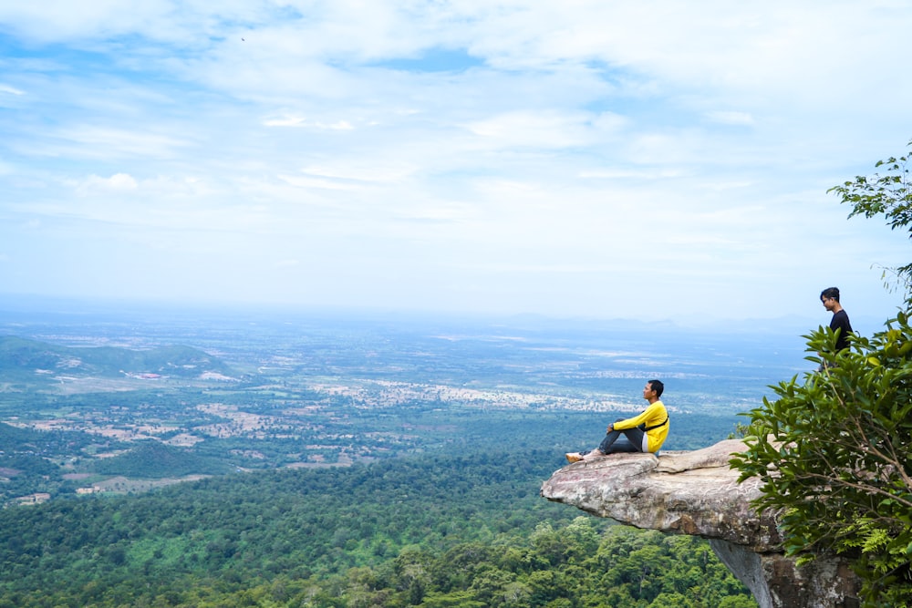 man in yellow shirt sitting on rock during daytime