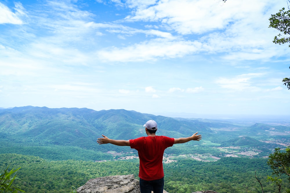 Mann im roten Hemd steht tagsüber auf dem Gipfel des Berges