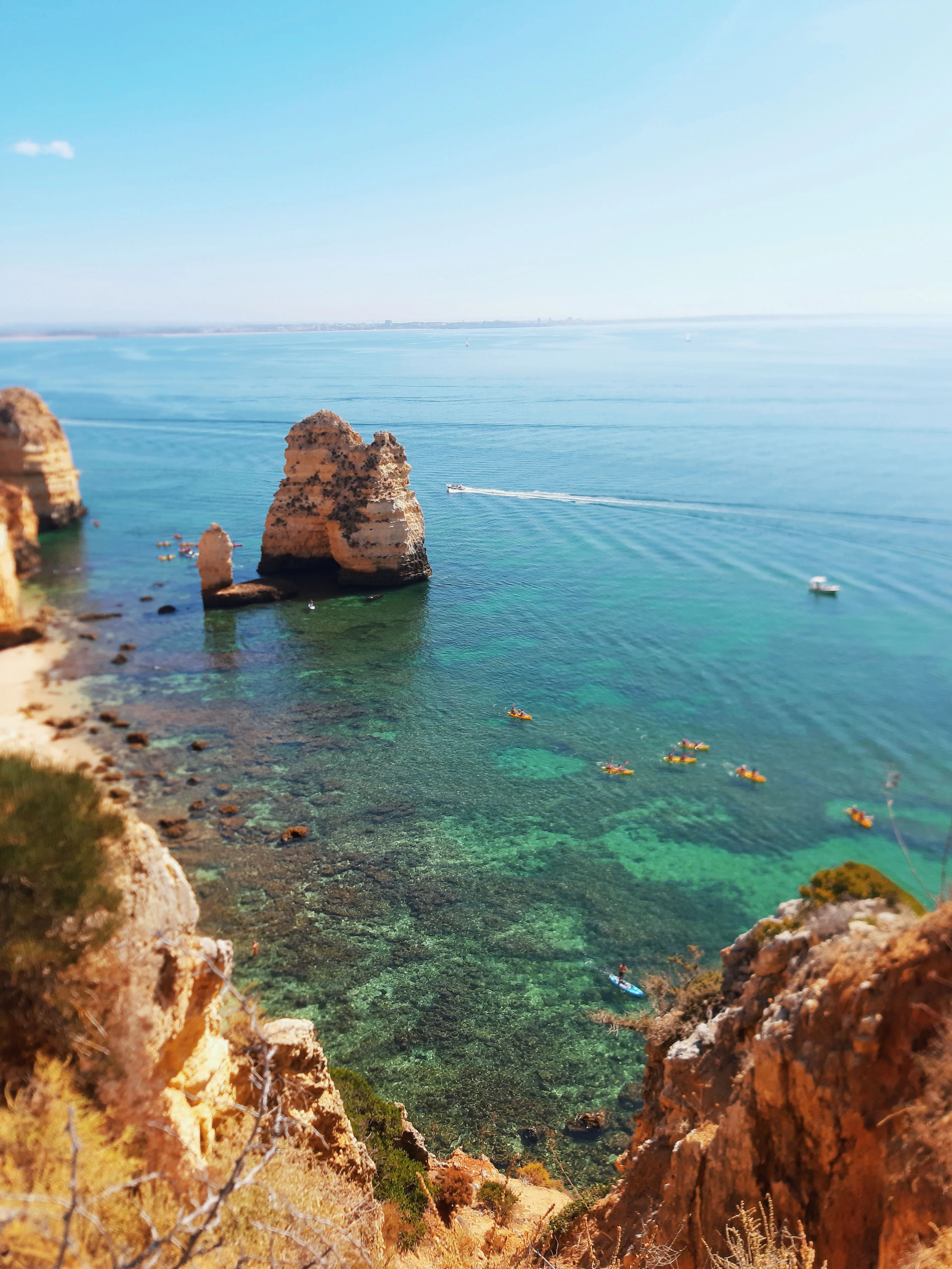 Ponta da Piedade near Lagos: golden sandstone sea stacks standing in clear turquoise water, with kayakers paddling in a group and a boat trailing a wake offshore
