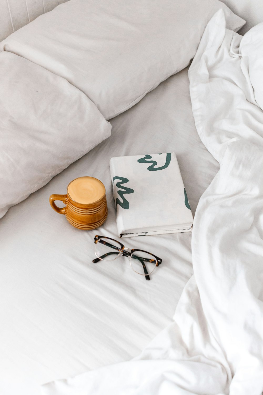 black framed eyeglasses beside brown ceramic mug on white textile