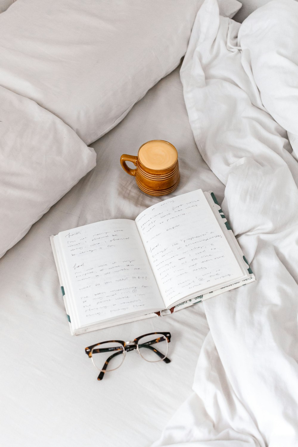 black framed eyeglasses on white book page beside brown ceramic mug on white textile