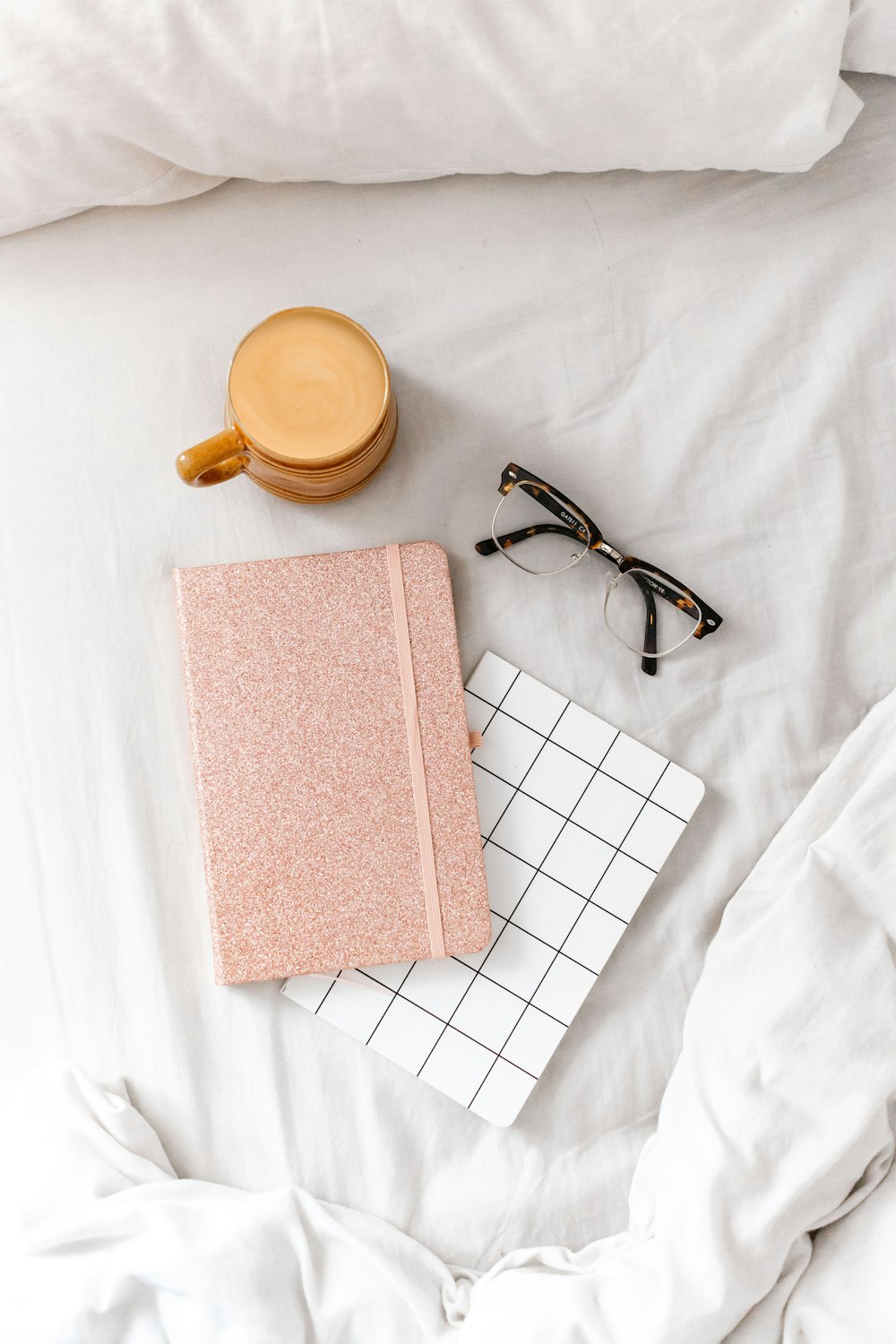 black framed eyeglasses beside brown book on white textile