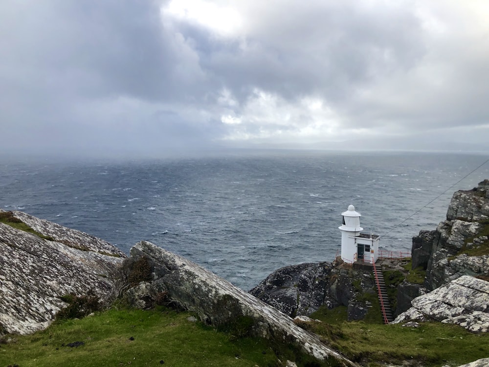 white and red lighthouse on green grass field near body of water under white clouds during