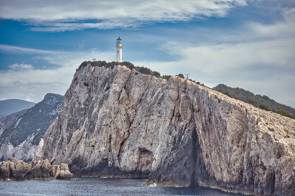 white lighthouse on brown rock formation beside body of water during daytime