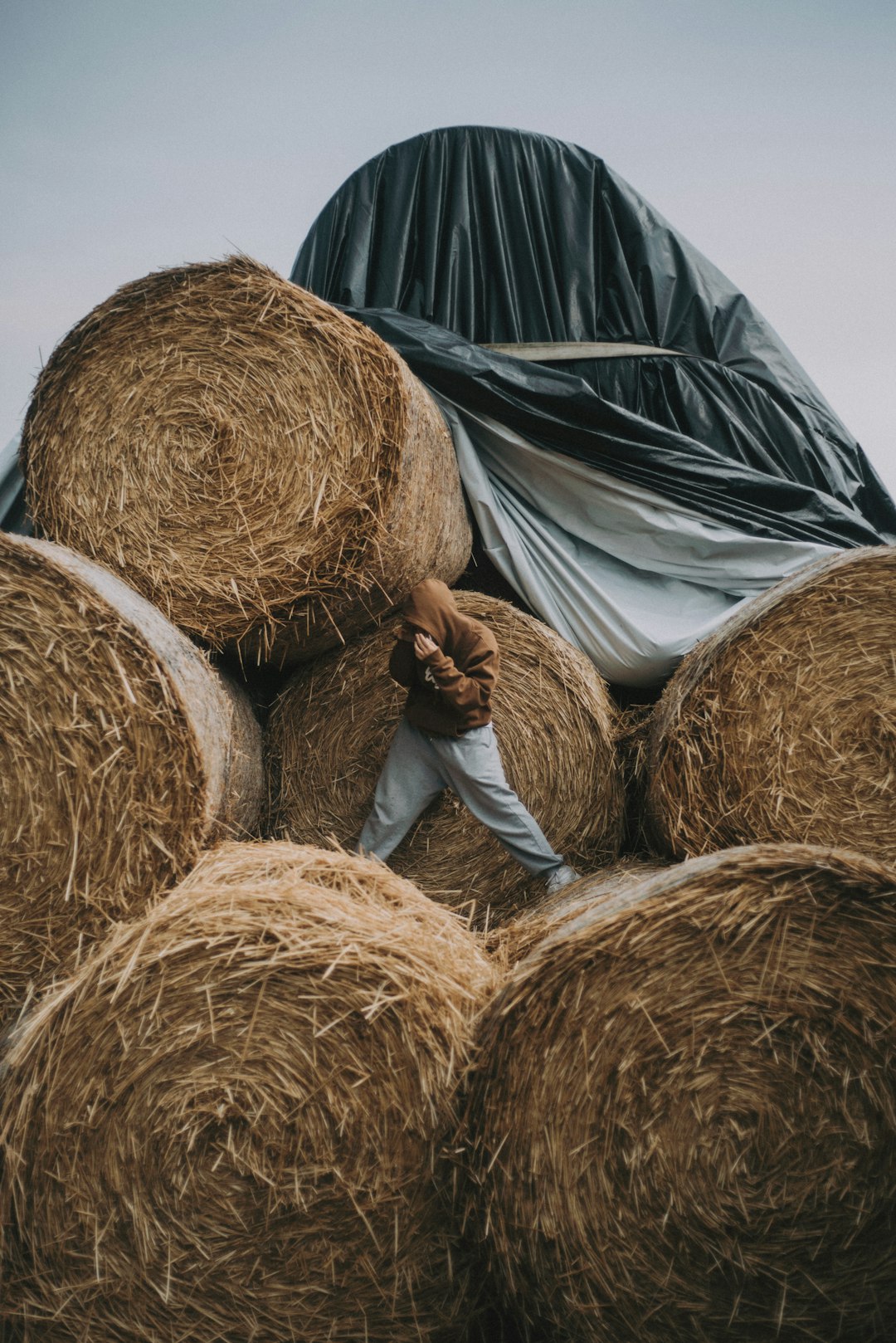 person in white shirt and black pants lying on brown hay rolls