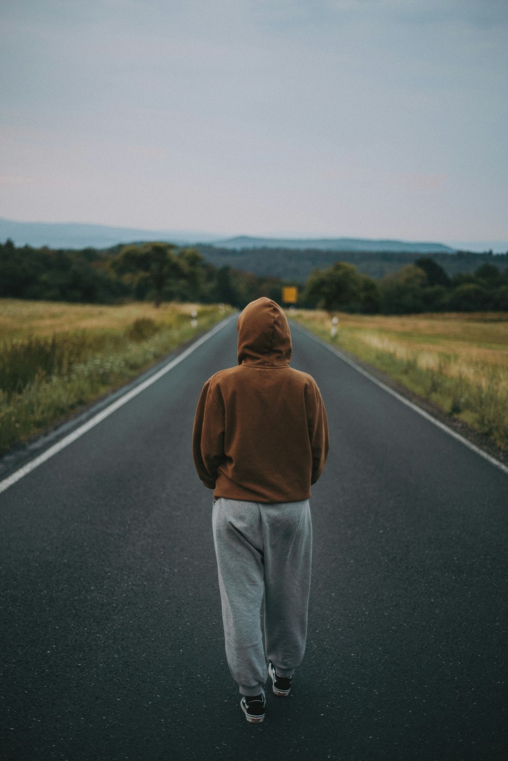 man in brown hoodie standing on road during daytime