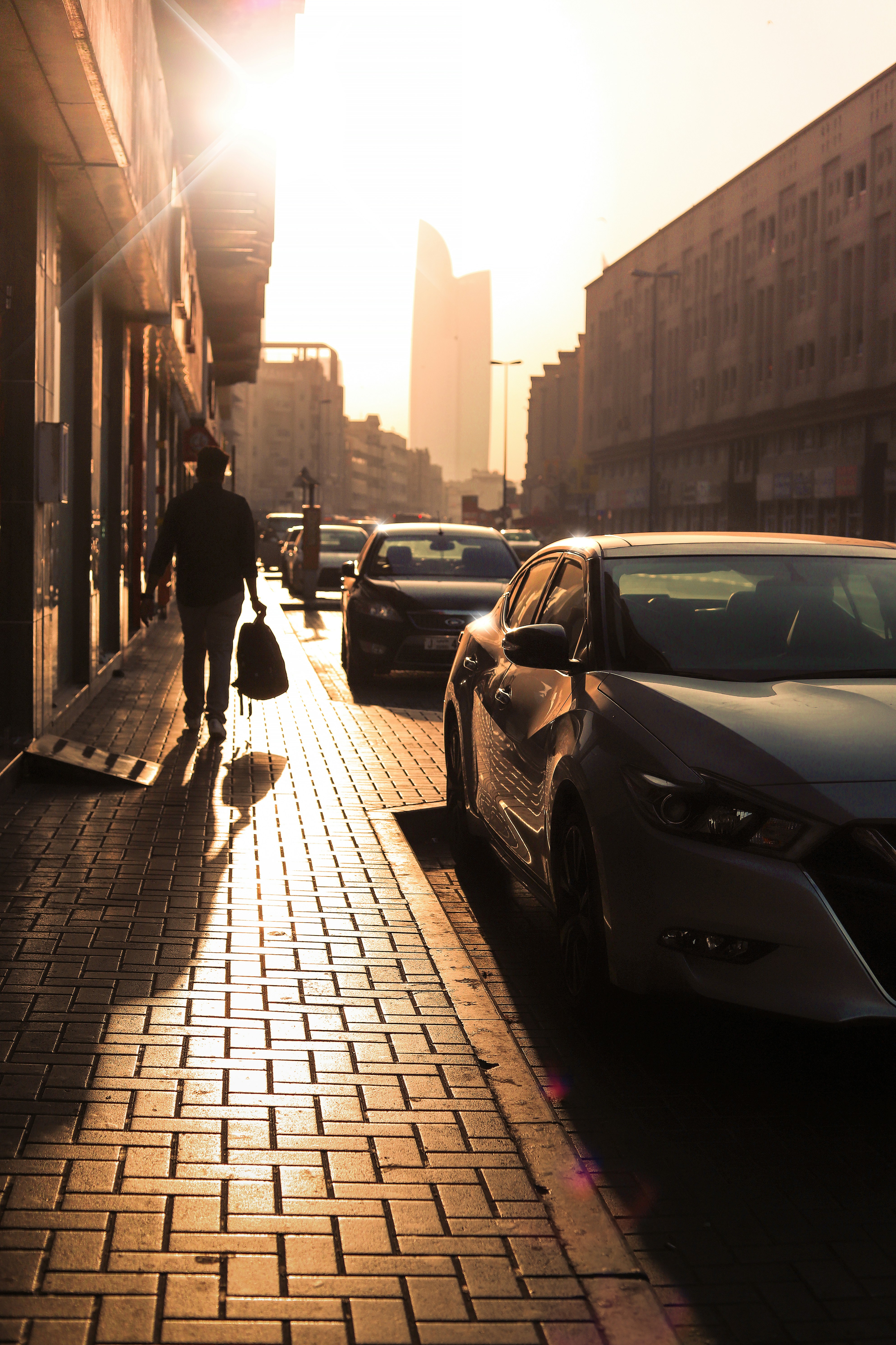 man in black jacket and pants walking on sidewalk during daytime