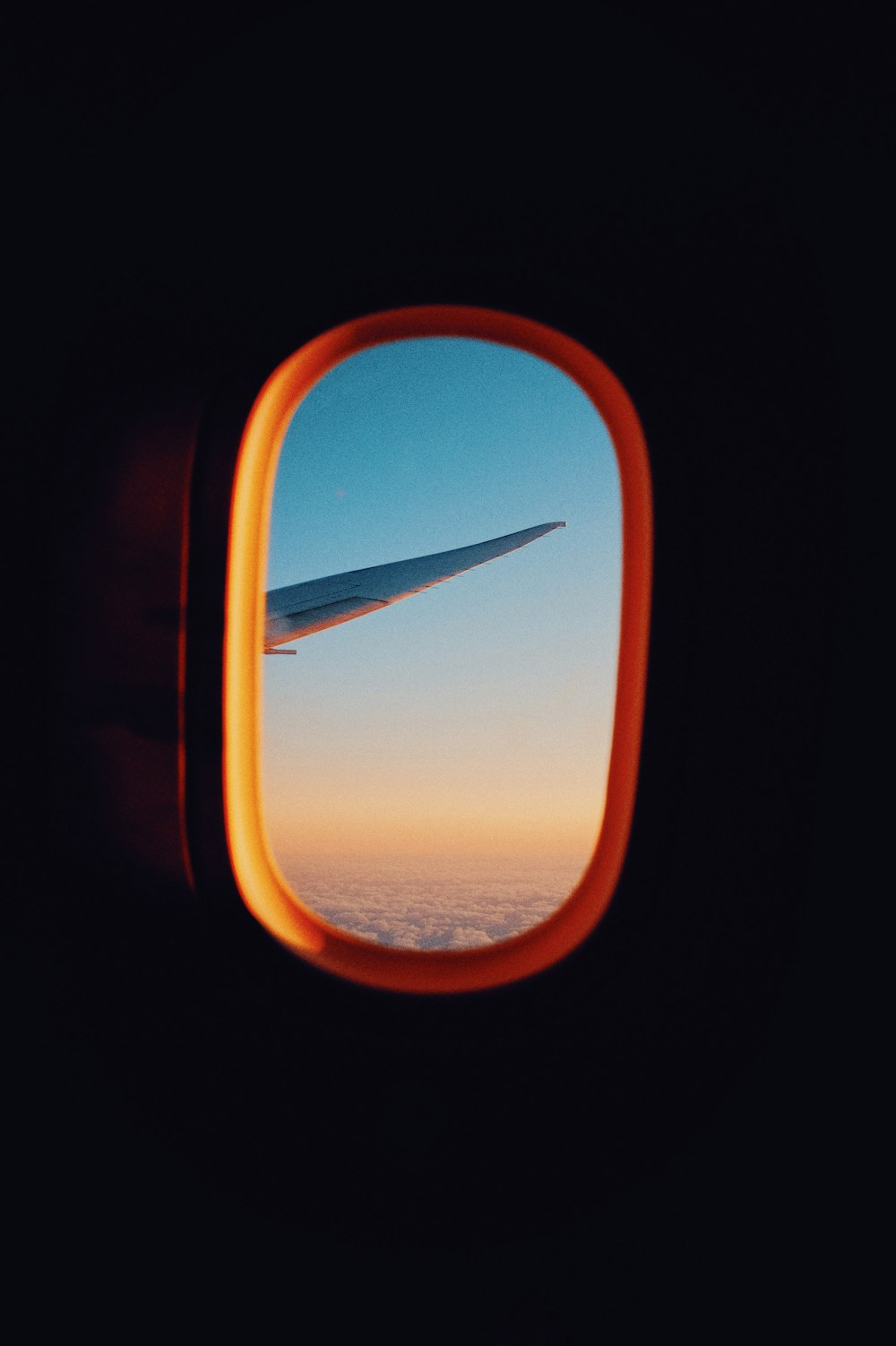 Flugzeugfenster Blick auf orange und weiß bewölkten Himmel während des Tages