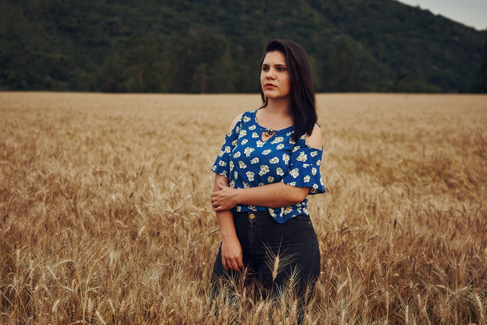 woman in blue and white floral shirt standing on brown grass field during daytime