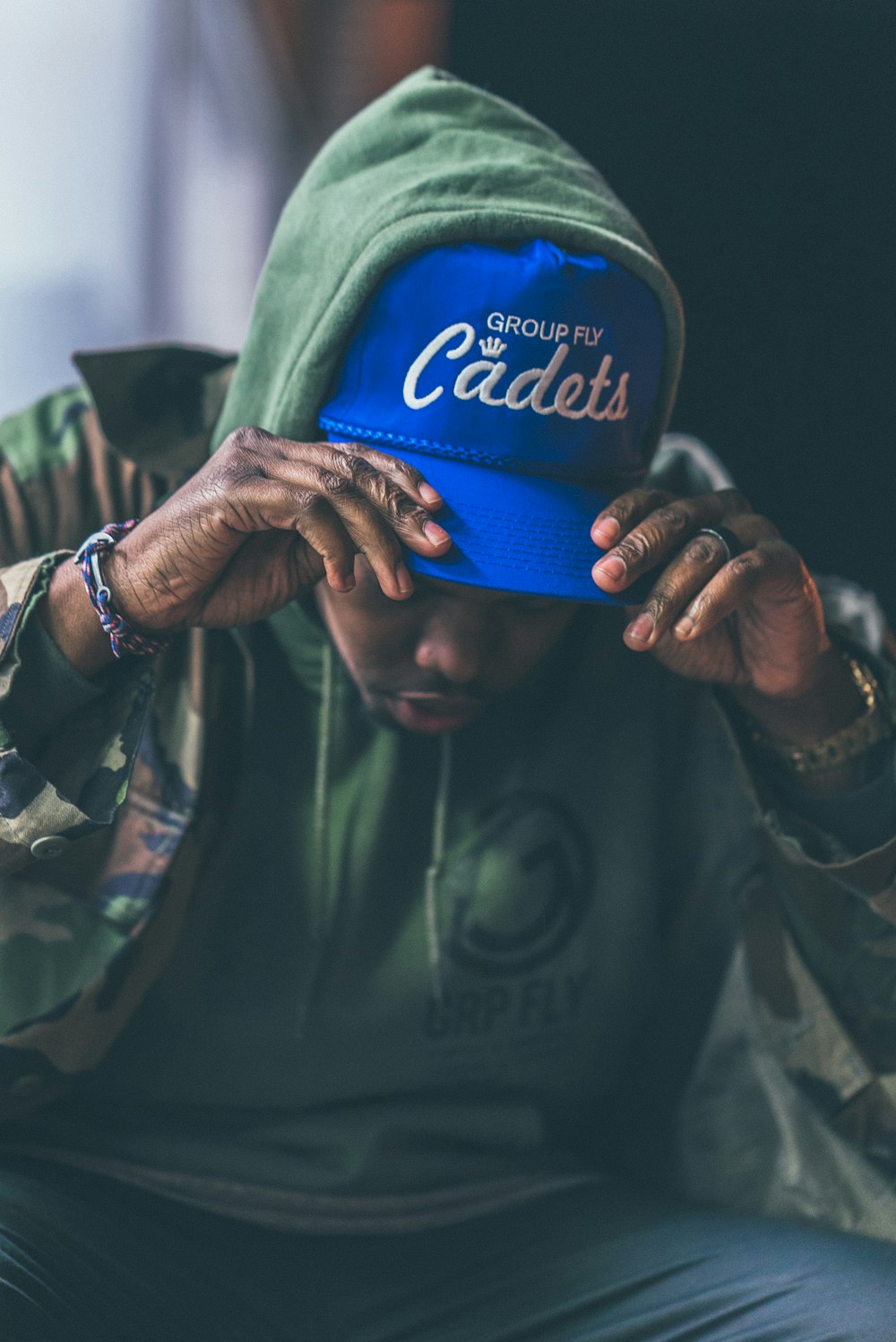 man in green and black camouflage jacket holding blue and white fitted cap