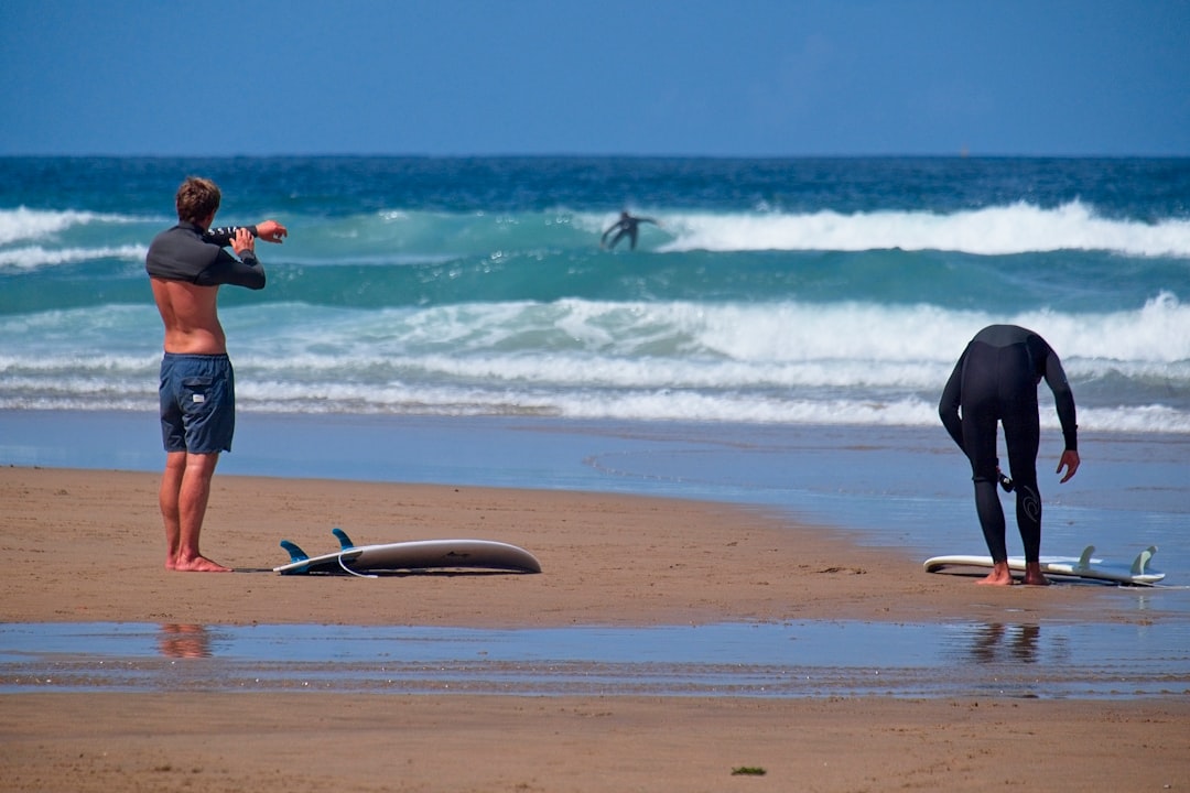 man in black shorts and black shirt holding black surfboard on beach during daytime