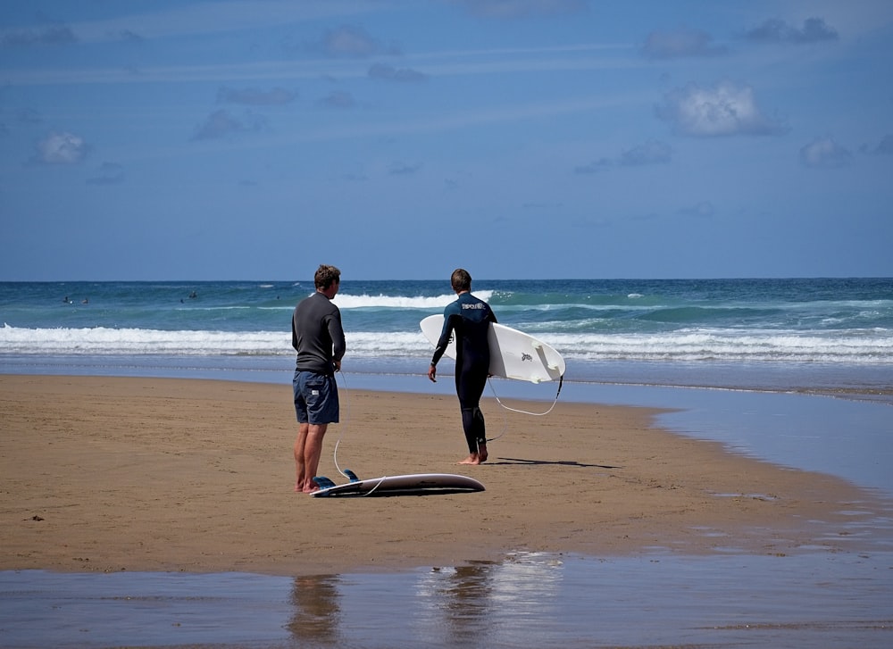 man and woman holding white surfboard walking on beach during daytime