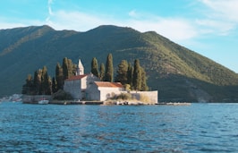 white and brown concrete house near body of water and green mountain during daytime