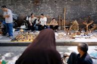 Smiling artisans chatting warmly with visitors around wooden craft displays outdoors.