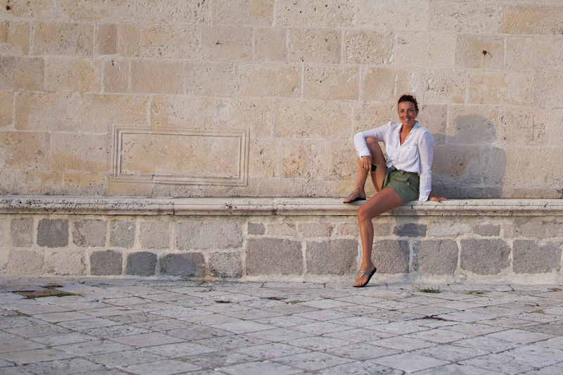 woman in white t-shirt sitting on concrete brick wall