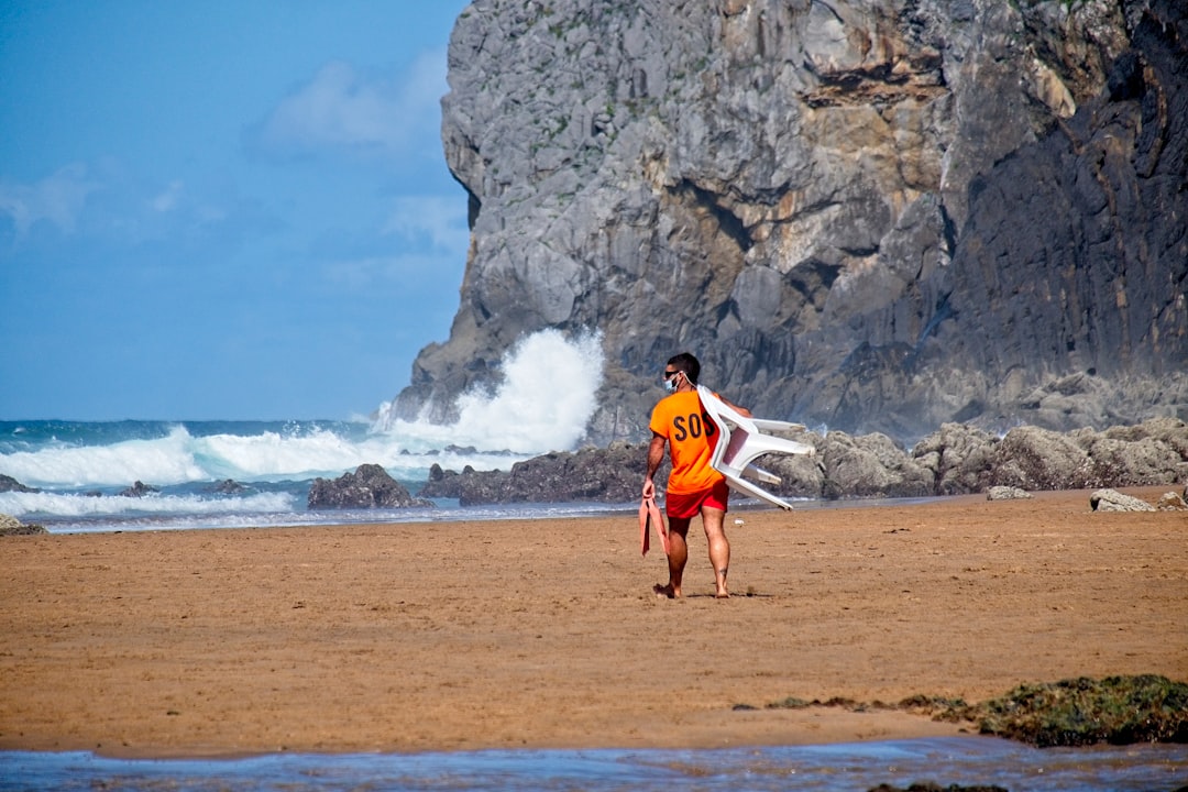 man in red shirt and blue shorts walking on beach shore during daytime