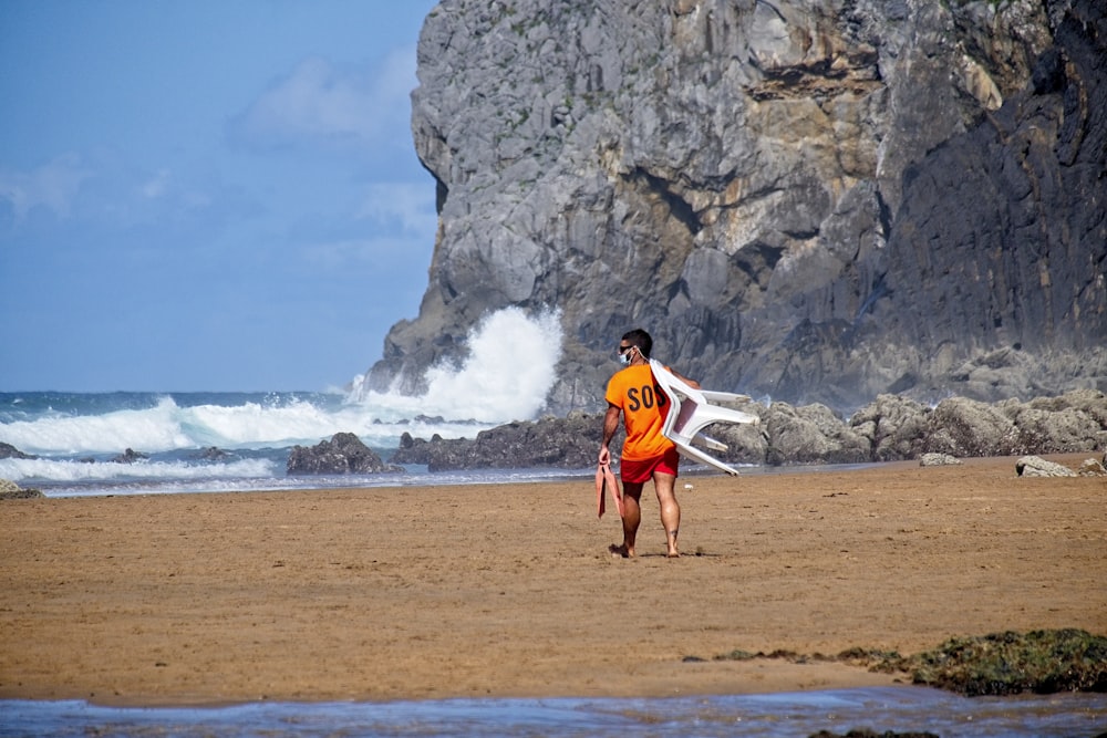 Uomo in camicia rossa e pantaloncini blu che cammina sulla spiaggia durante il giorno