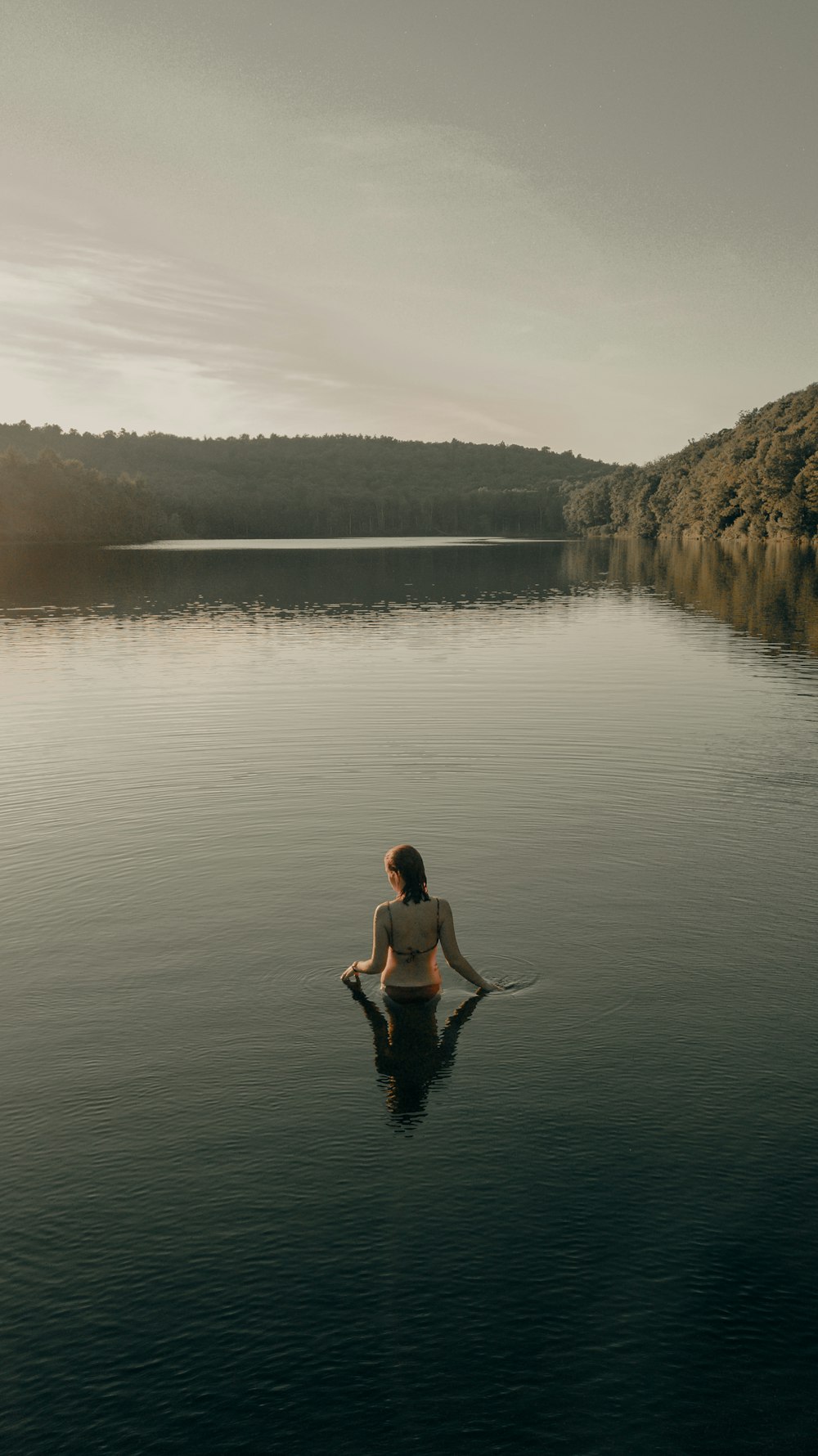 Mulher no biquíni preto sentado na rocha perto do corpo de água durante o dia