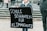 A person is holding a black protest sign with white text that reads 'Schule schwänzen für Klimaschutz' which translates to 'Skipping school for climate protection'. The surroundings indicate an outdoor public space, possibly during a demonstration or protest.
