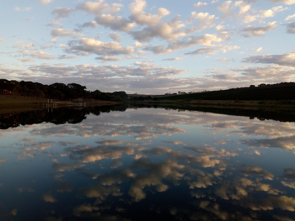 body of water near green grass field under blue sky and white clouds during daytime