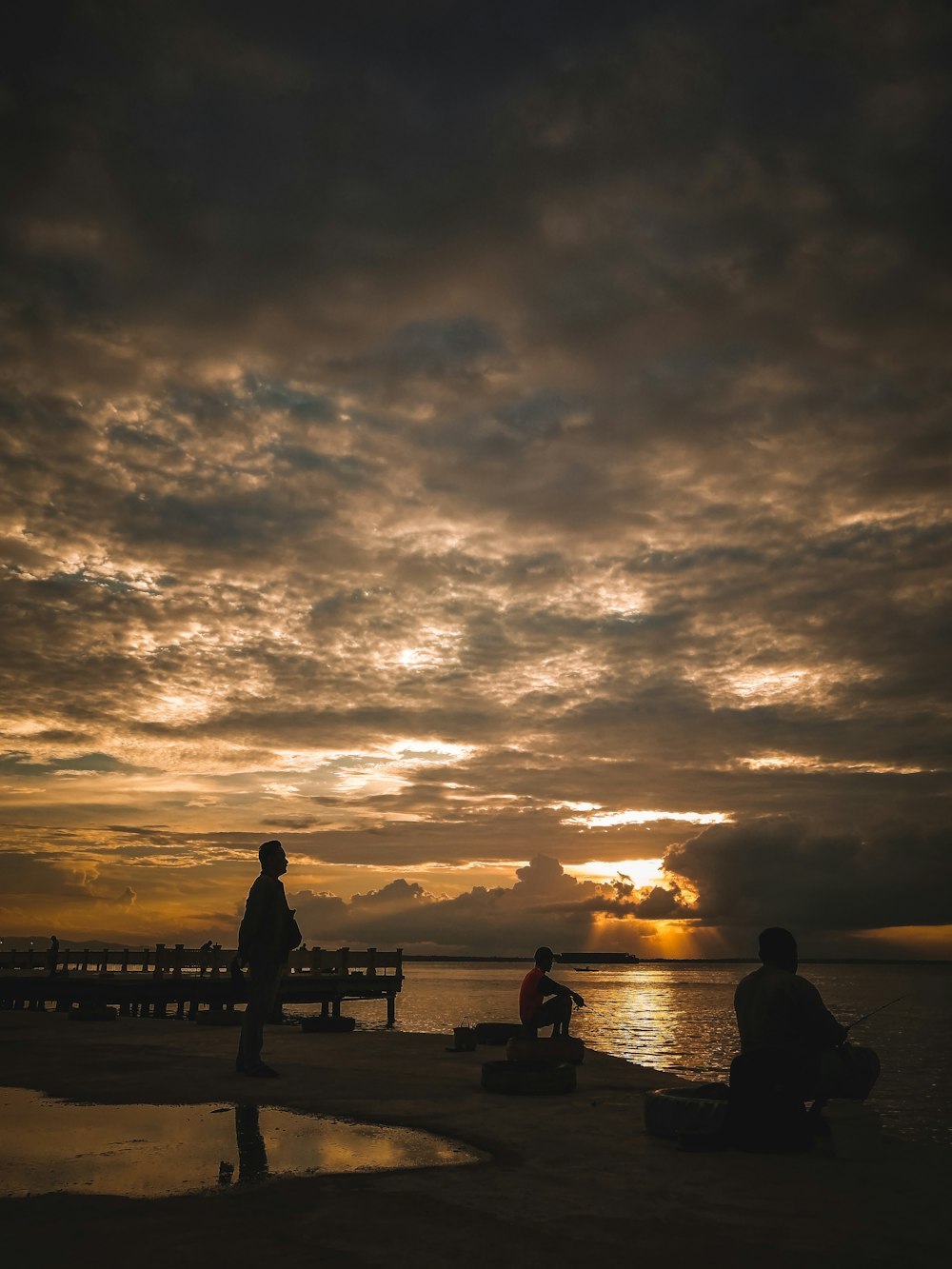 silhouette of people standing on dock during sunset