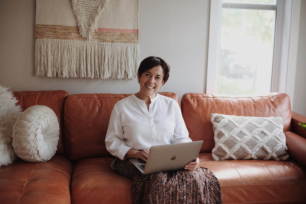 man in white dress shirt sitting on red couch using silver macbook