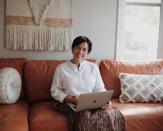 man in white dress shirt sitting on red couch using silver macbook