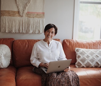 man in white dress shirt sitting on red couch using silver macbook