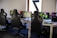 A row of gaming stations equipped with large monitors, gaming chairs, keyboards, and headphones. The setup is organized and ready for gaming, featuring a colorful screen display. The room has a modern and tech-savvy ambiance.