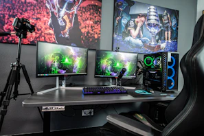 A gaming desk with two monitors, a computer tower, and a camera on a tripod