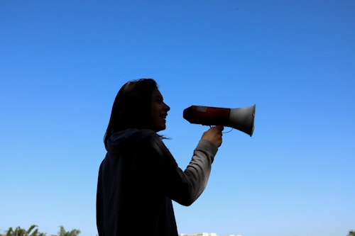 A silhouette of a person holding a megaphone against a clear blue sky, suggesting communication or a call to action.