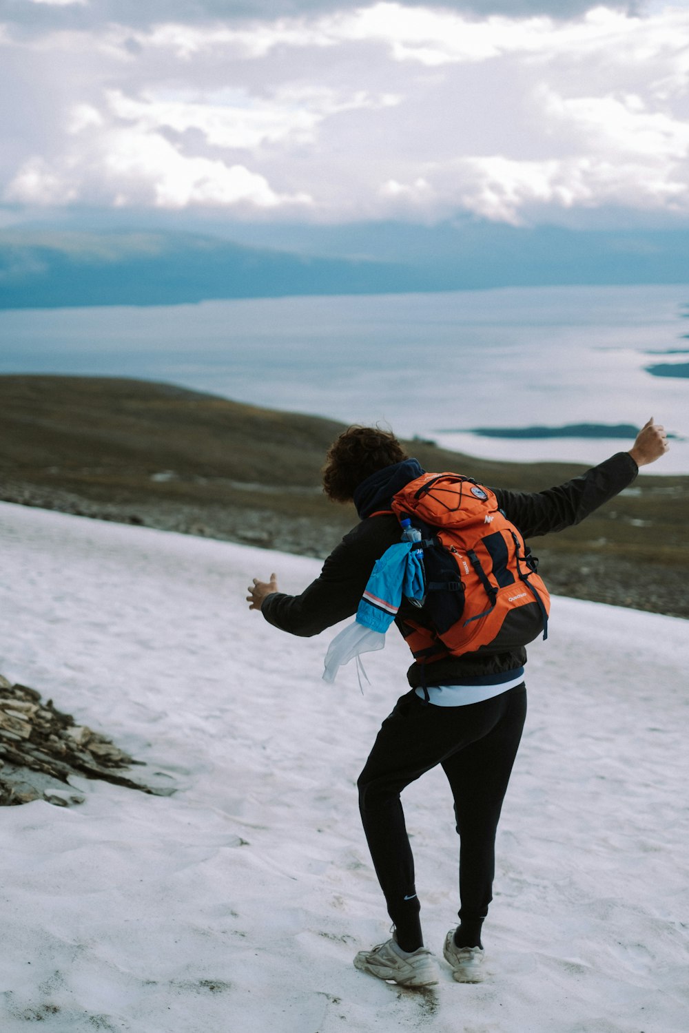 woman in orange and black jacket and black pants standing on snow covered ground during daytime