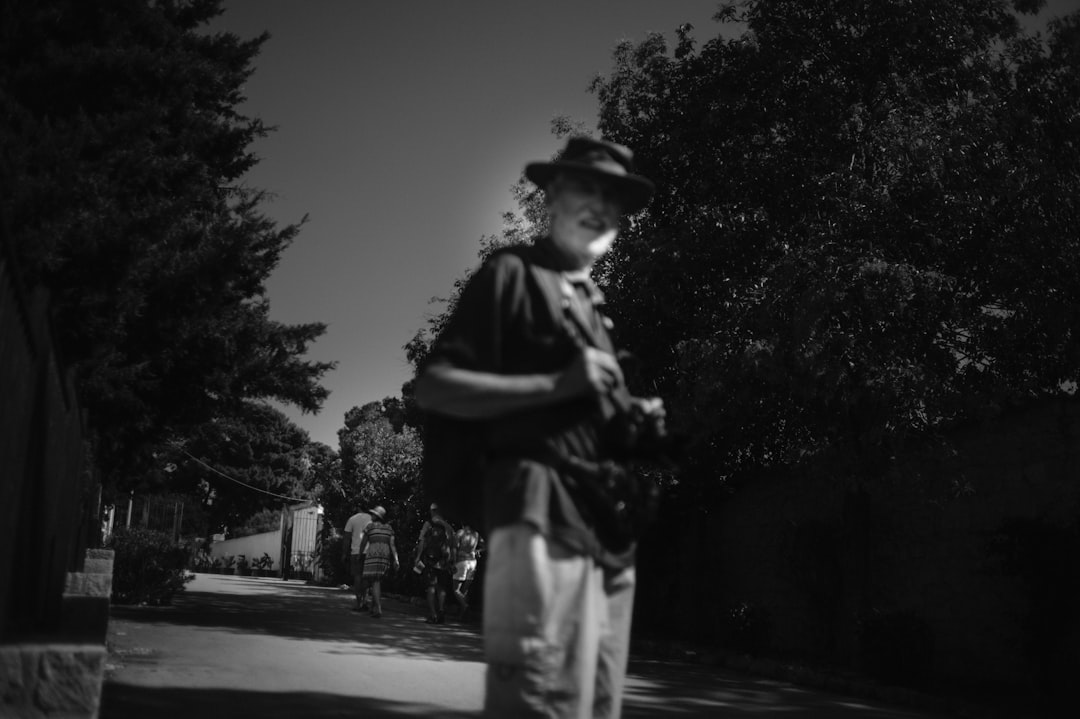 man in black jacket and pants standing on road in grayscale photography