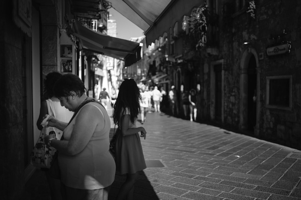 grayscale photo of woman in white tank top and black skirt standing on sidewalk