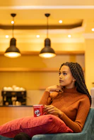Lifestyle shot of a woman seated in a cozy coffee shop wearing a black reminder tee, surrounded by warm ivory tones.