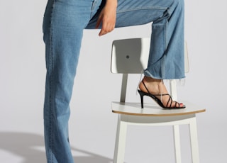 woman in white tank top and blue denim jeans sitting on white chair