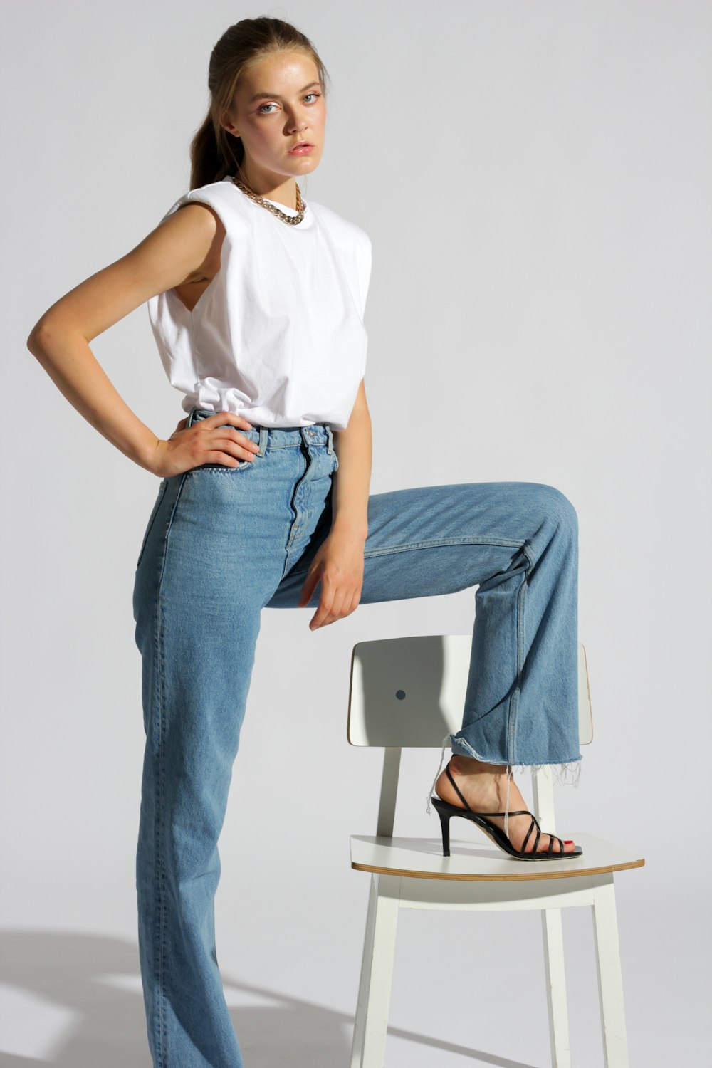 woman in white tank top and blue denim jeans sitting on white chair